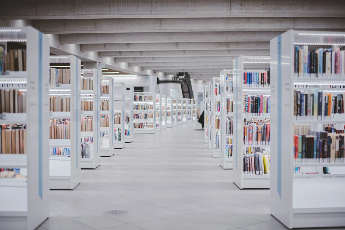 Allée de bibliothèque aux rayonnages blancs, baignée de lumière