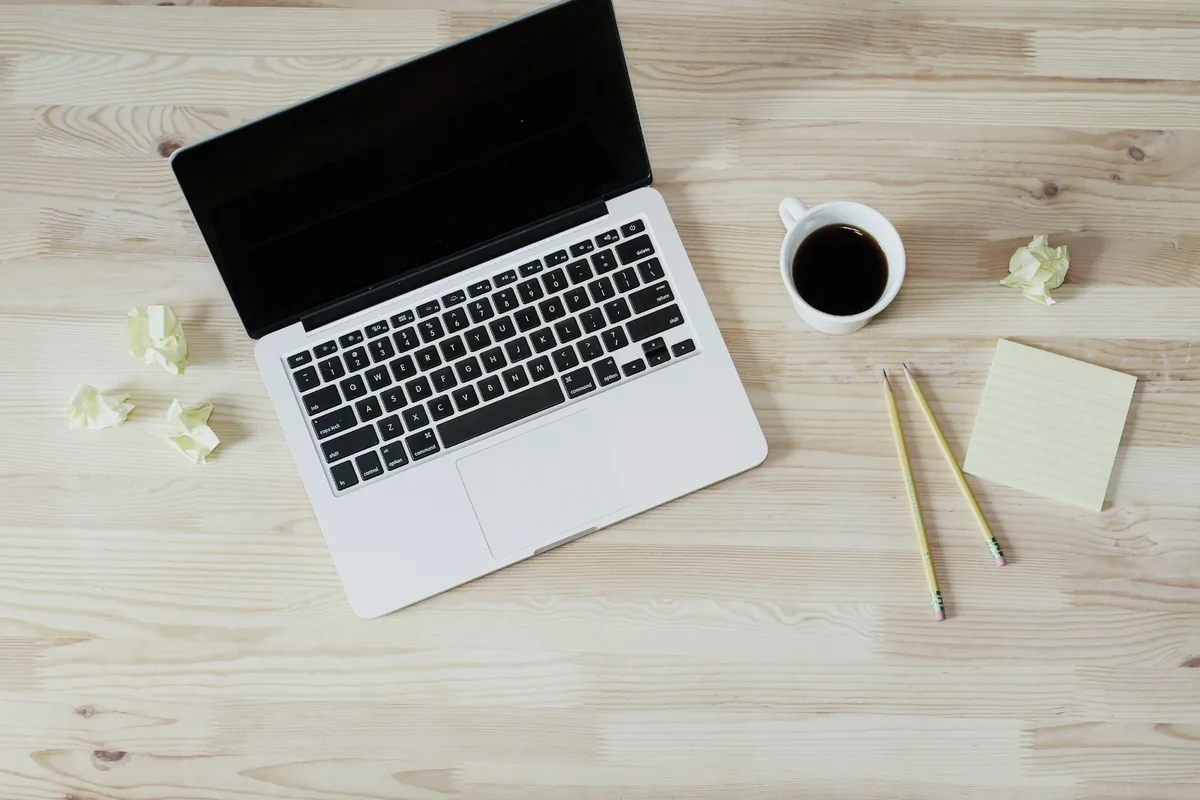 Plan de travail en bois clair vu du dessus : ordinateur portable, tasse de café et notes