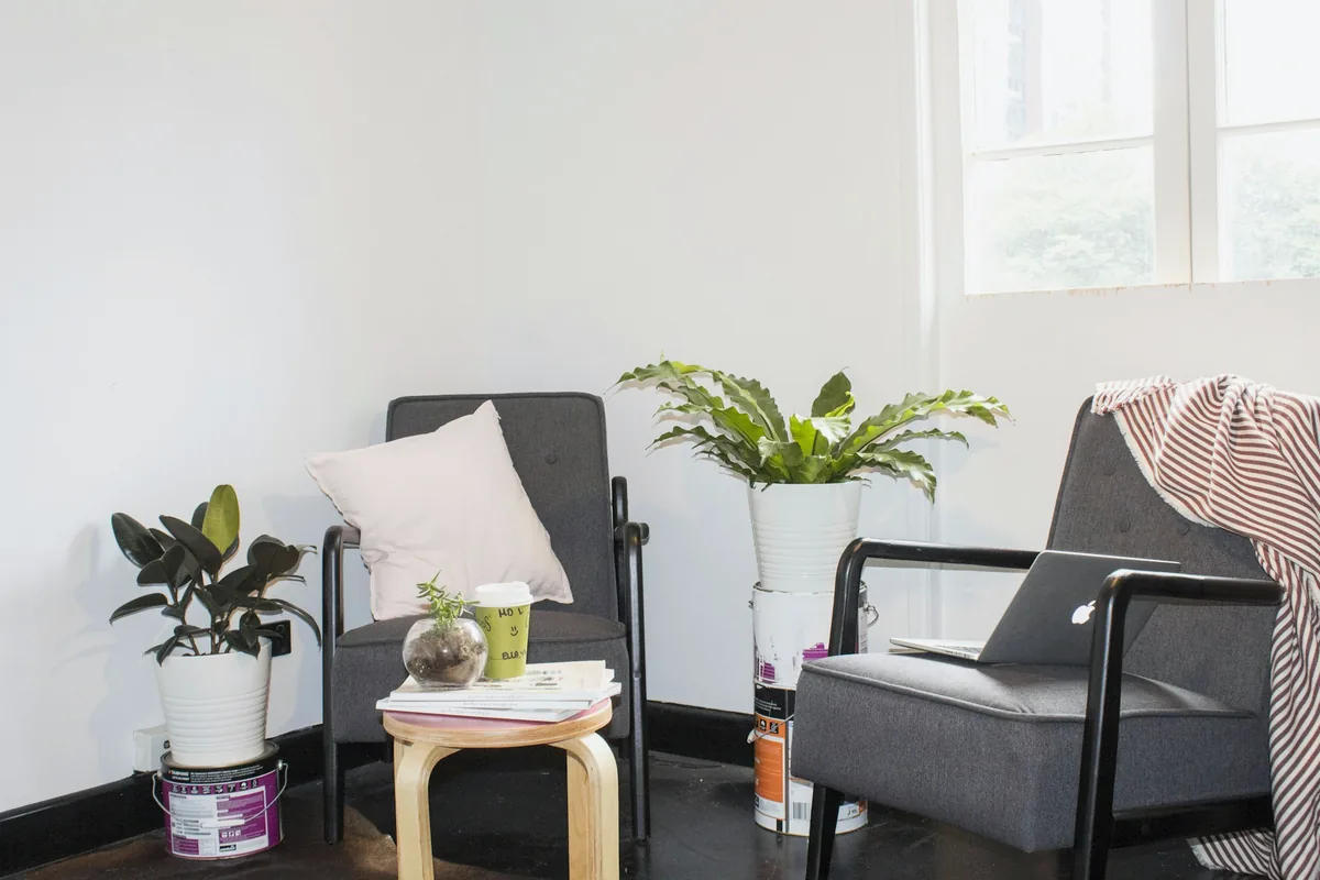 Deux fauteuils gris, des plantes vertes et une petite table près d'une fenêtre claire