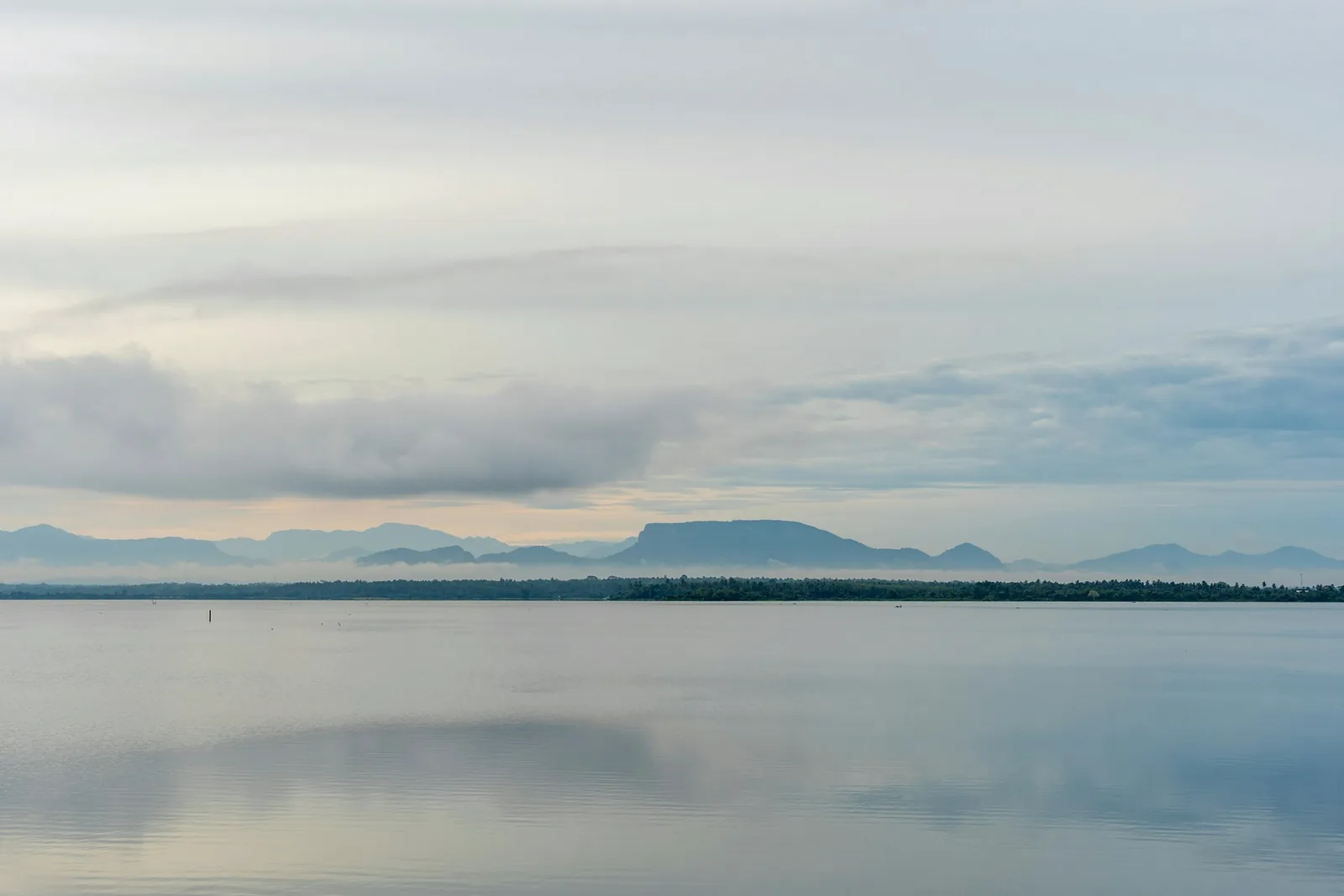 Surface d'un lac calme sous un ciel voilé, montagnes lointaines à l'horizon