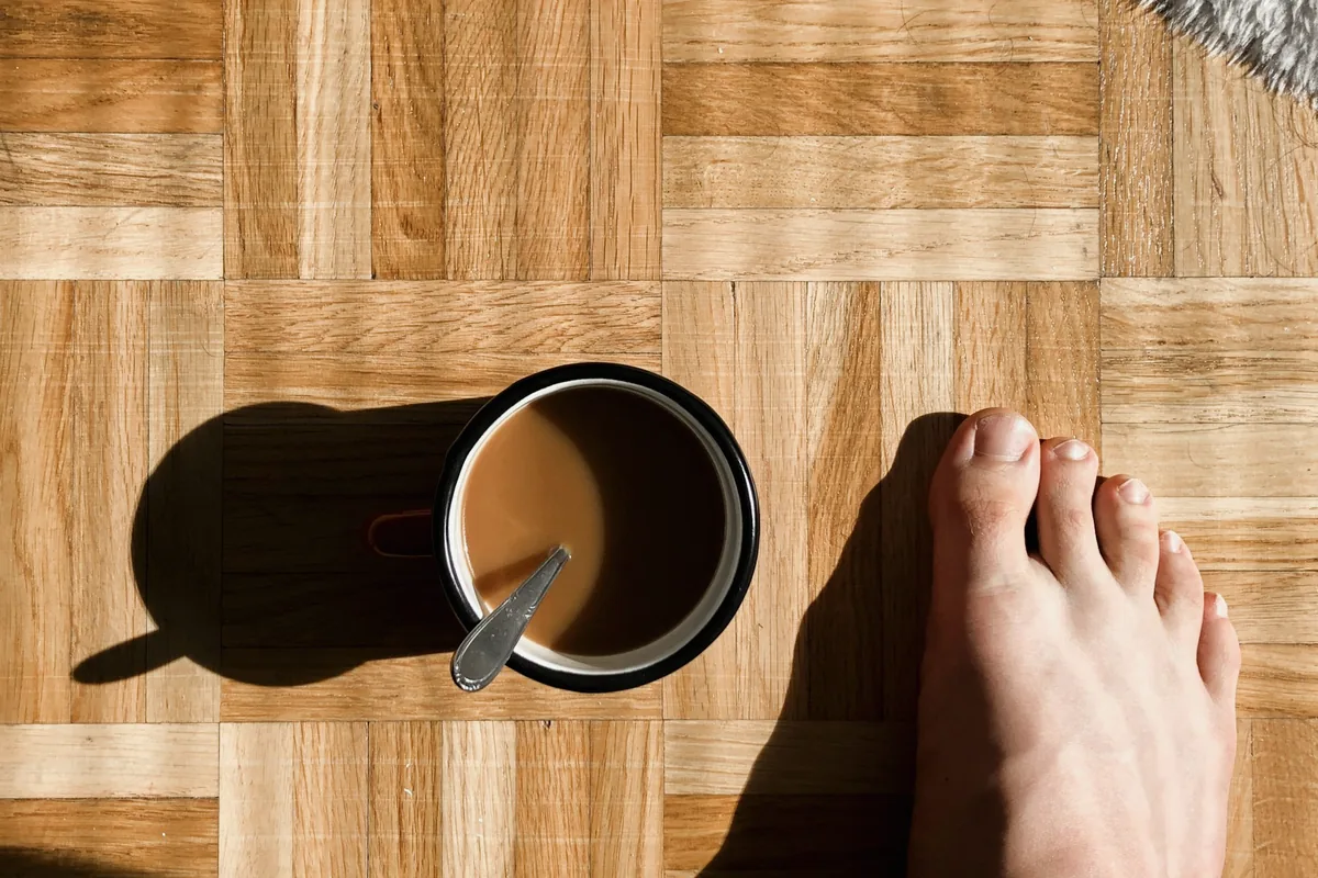 Vue de dessus d'un pied nu posé sur un parquet clair, à côté d'une tasse
