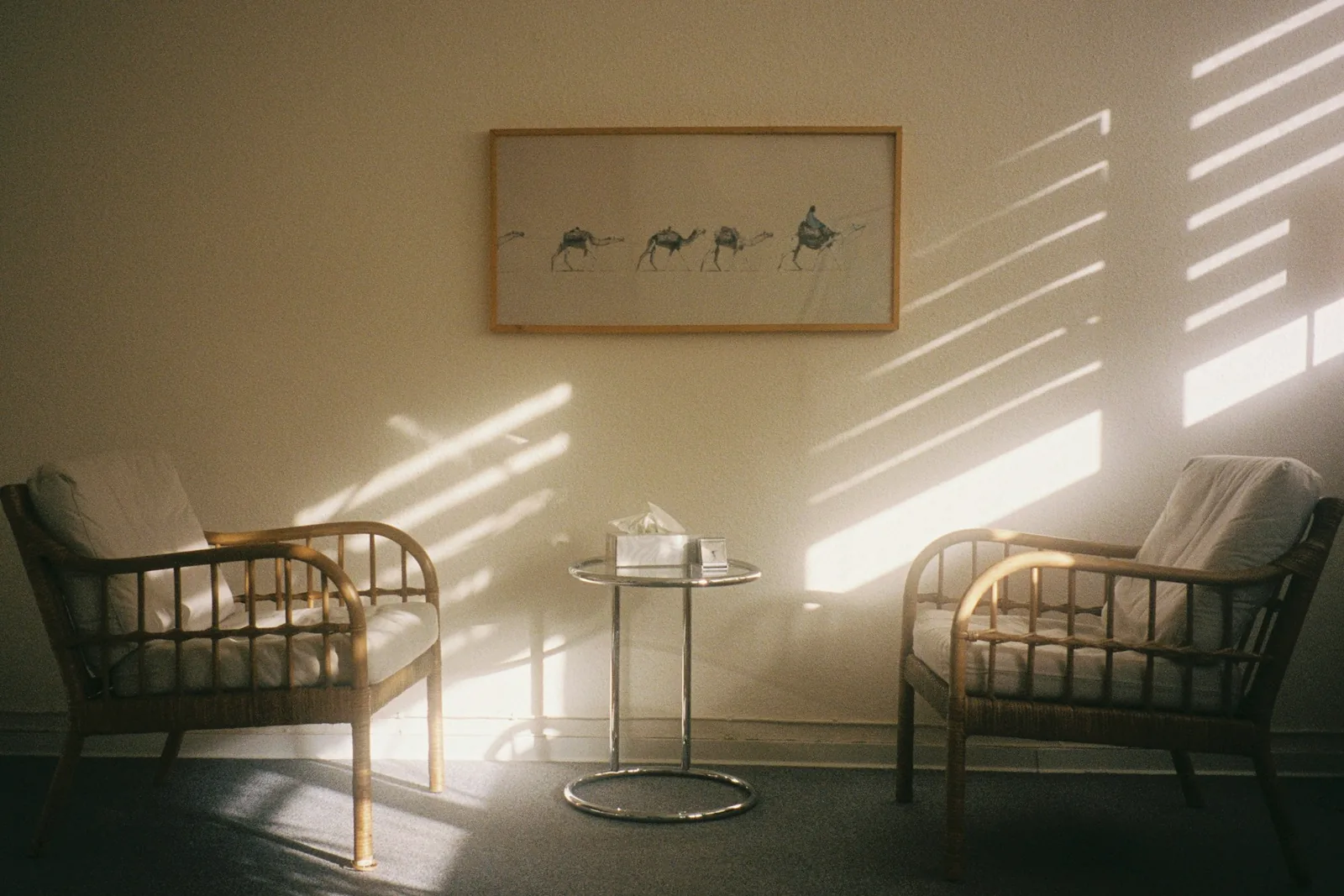 Salle calme baignée d'une lumière rasante, deux fauteuils en rotin face à une petite table